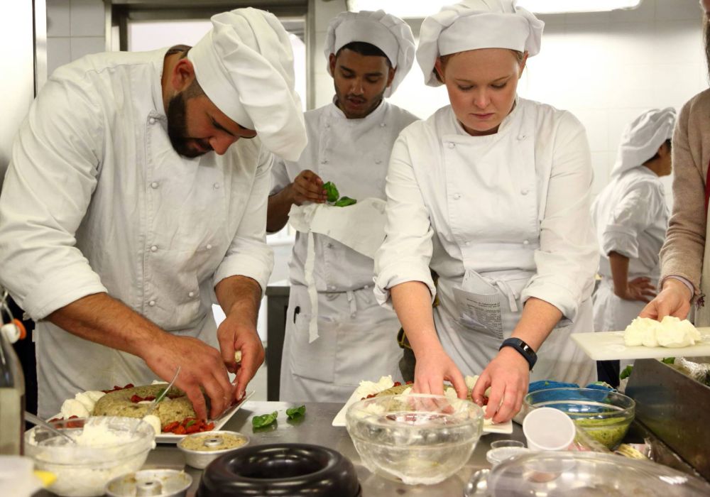 A group of culinary students in a kitchen, focused on preparing various dishes together.
