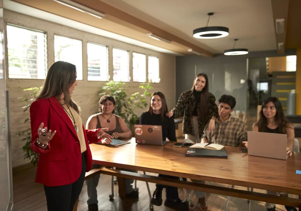 A woman in a red jacket presenting to her students.
