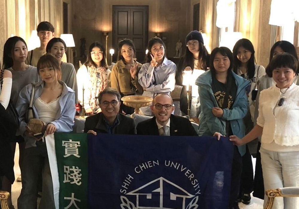 Students at Shih Chien University in Taiwan posing together with a banner for a photo.