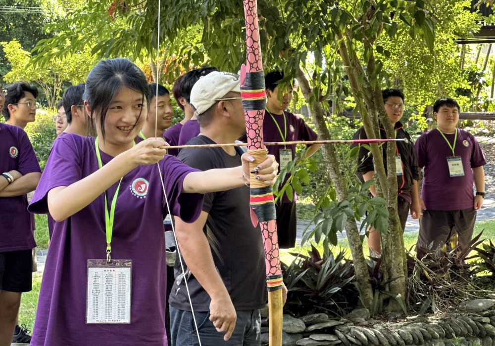 A student aims a bow and arrow, focused and ready to shoot.