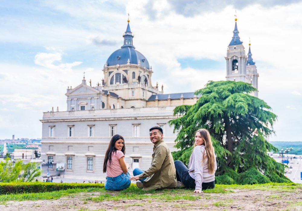 Three individuals seated on the grass, enjoying the view of a majestic cathedral.